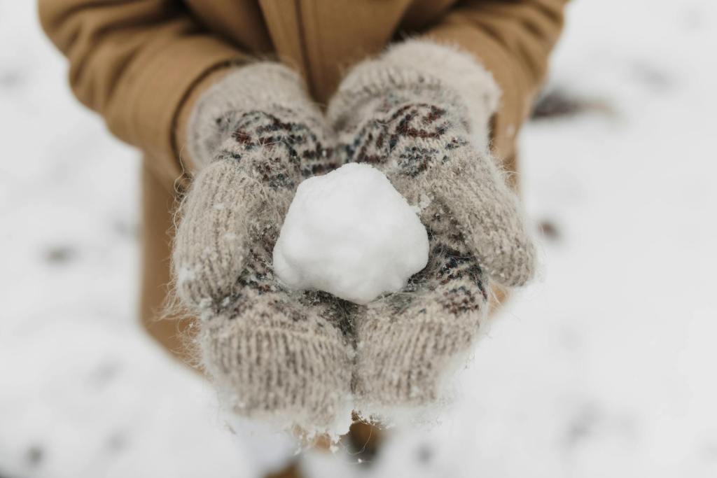 Ett par vita tumvantar som håller i en snöboll