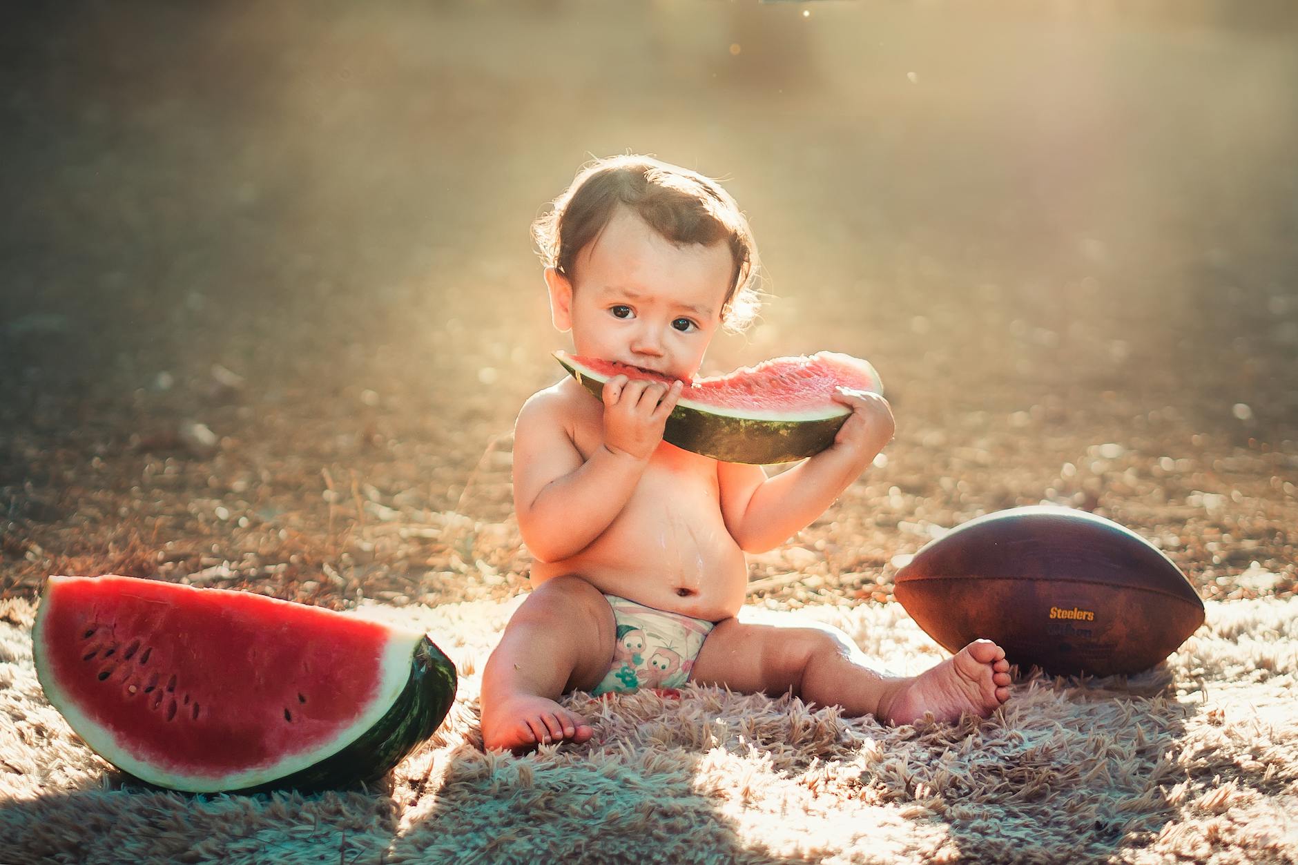 En bebis som sitter utomhus på en filt och äter en stor vattenmelon